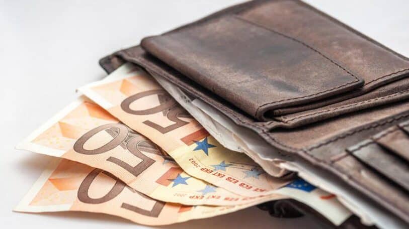 ένα δερμάτινο καφέ πορτοφόλι είναι ακουμπισμένο σε επιφάνεια και από μέσα του εξέχουν τρια 50ευρα - ΔΥΠΑ: Επίδομα 1.760 ευρώ μόνο με ένα δικαιολογητικό